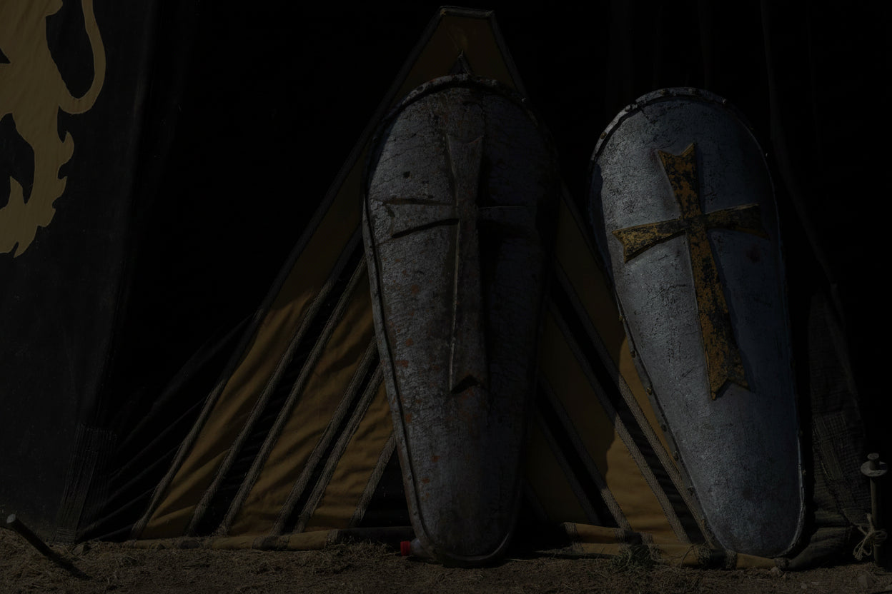 Two medieval shields with cross designs in front of a tent with lion emblem.